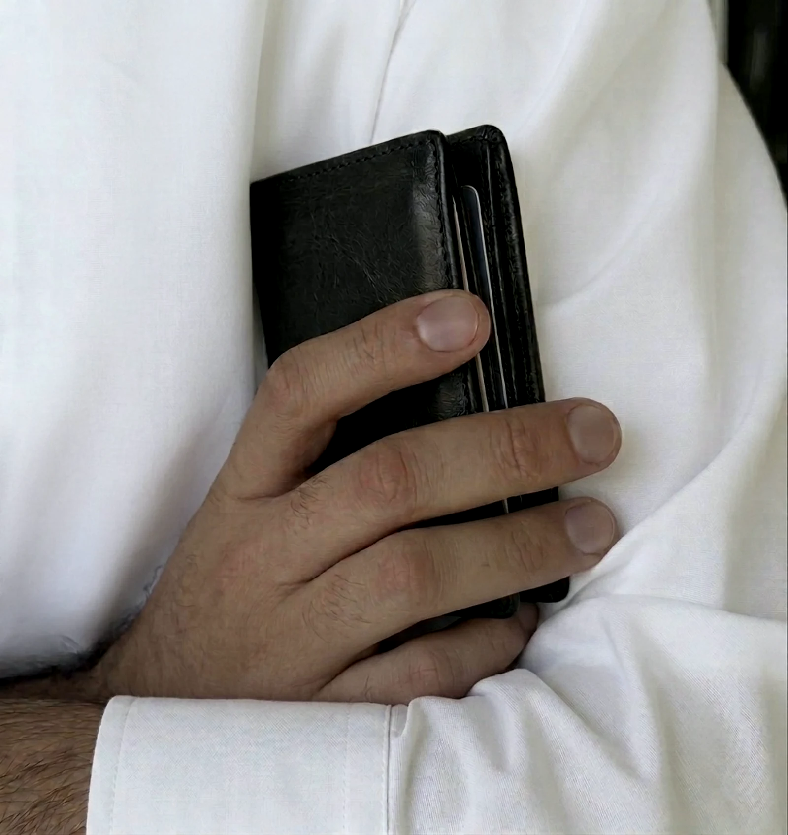 A man's hand with neatly groomed natural nails, holding a leather wallet