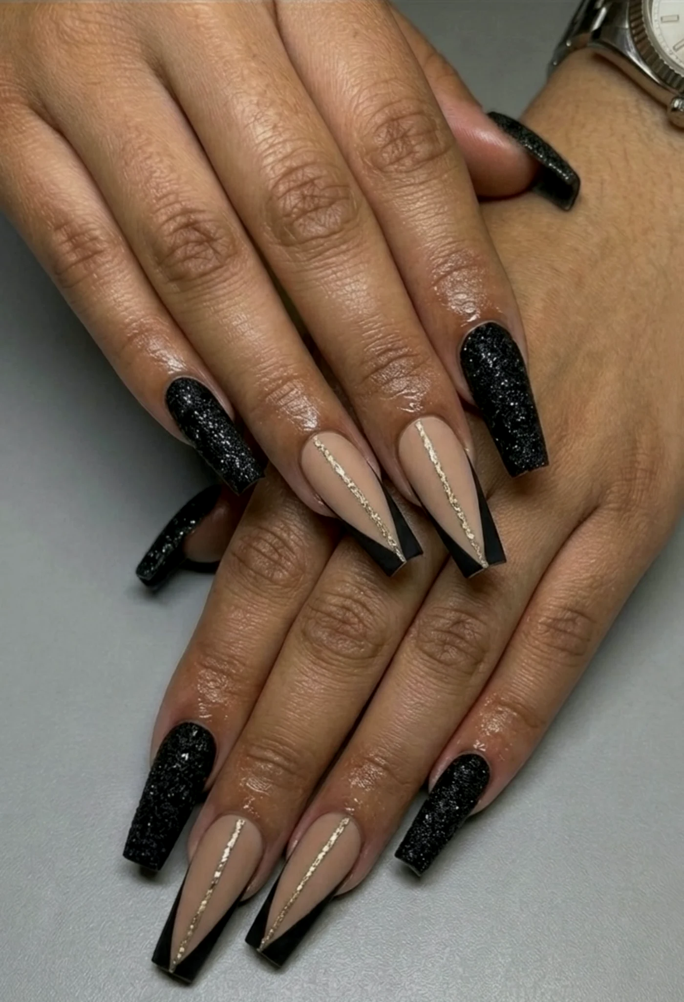 Long coffin-shaped nail extensions in black glitter and nude with fine gold lines